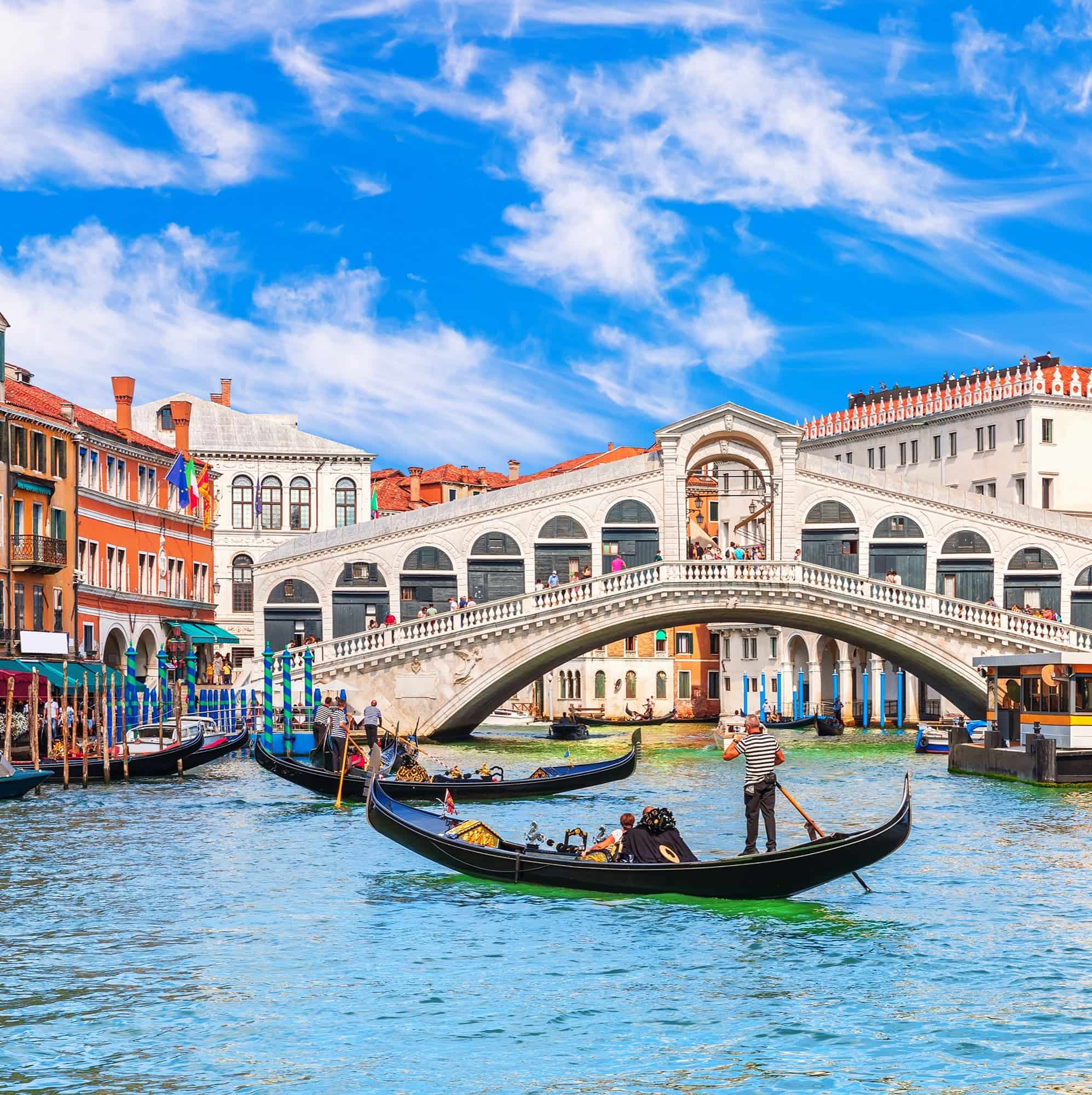 a man paddles accross a river in a gondola on a sunny day in venice