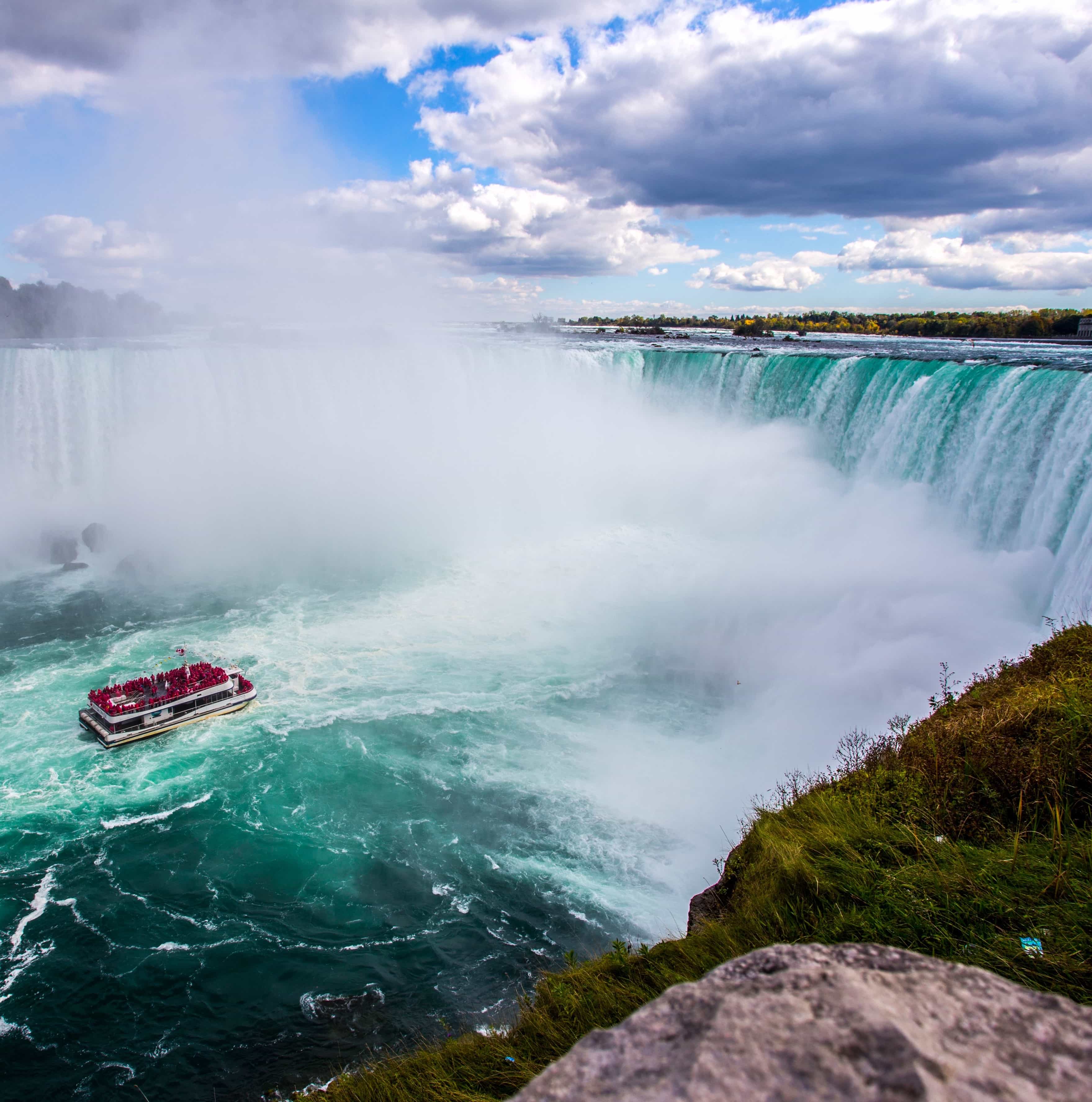 a small boat filled with passengers rides in close to a watefall in niagra falls