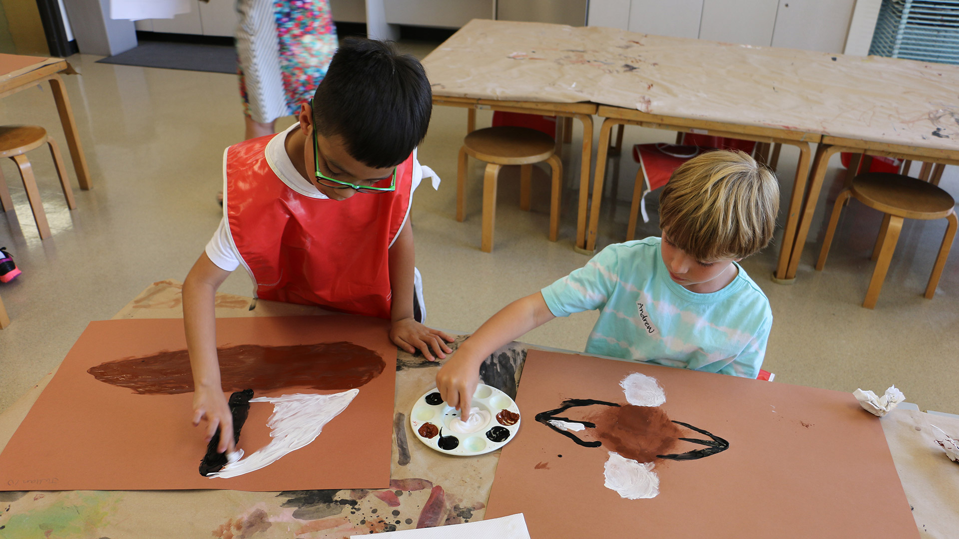 Two boys finger painting on a large sheet of brown paper.