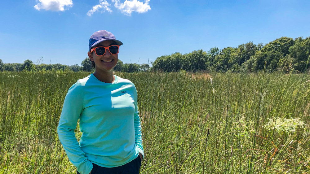 Angelica is standing in a prairie on a sunny day and smiling at the camera.
