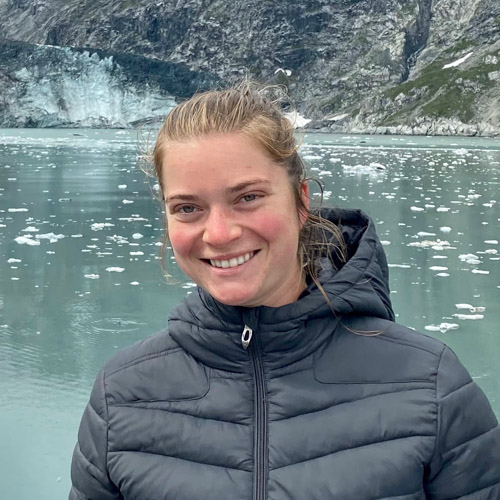 Isabel is smiling at the camera in front of a body of water with pieces of ice floating haphazardly.