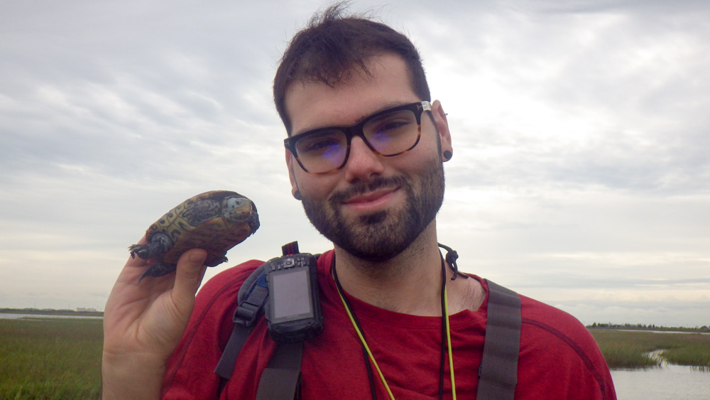 Randon is in a marsh holding up a diamondback terrapin.