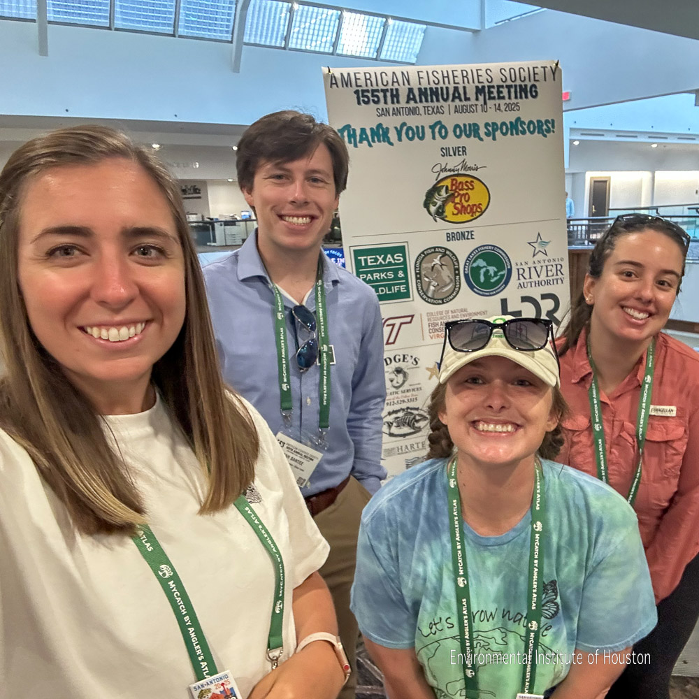 Four people pose for a group selfie in front of a conference banner.