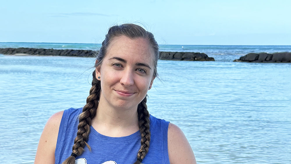 Kylie is smiling at the camera against an ocean backdrop, with jetties extending into the water