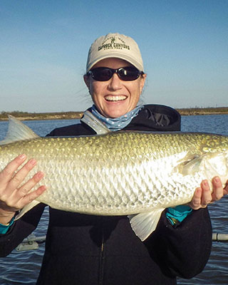 Jenny is smiling to the camera. She is holding a large fish out in front of her.