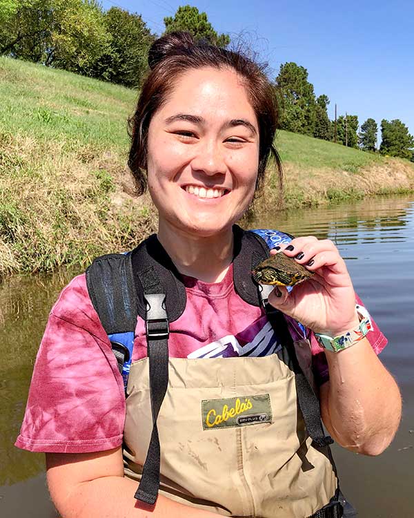 Robyn is holding a small aquatic turtle as she smiles into the camera.