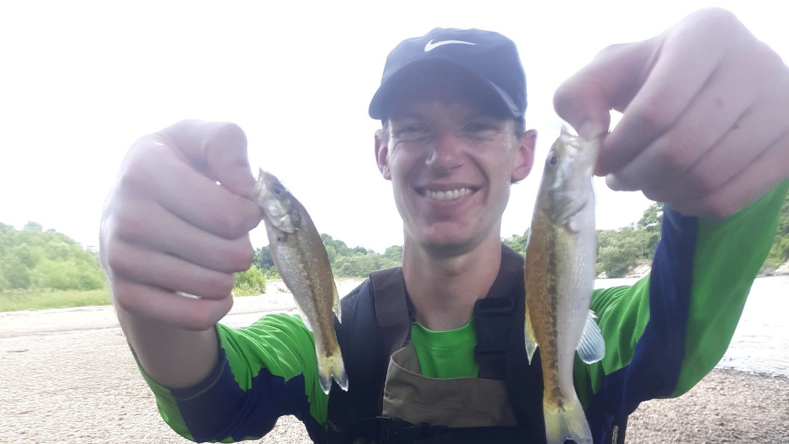 Aaron is holding two small fish up to the camera.