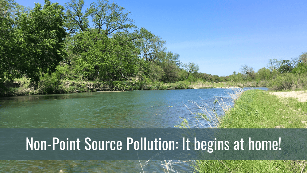 Non-Point Source Pollution: It begins at home! A calm river bordered by lush green trees and vegetation under a clear blue sky, with the water reflecting the surrounding greenery. Text overlay at the bottom reads: 'Non-Point Source Pollution: It begins at home!'