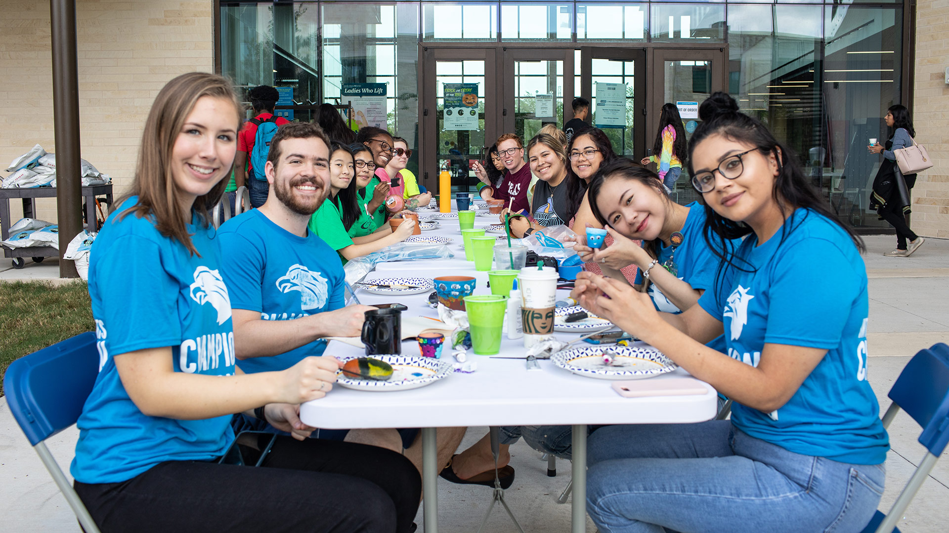 Students in blue UHCL shirts gathered at a Student Affairs activity table outside the Recreation and Wellness Center