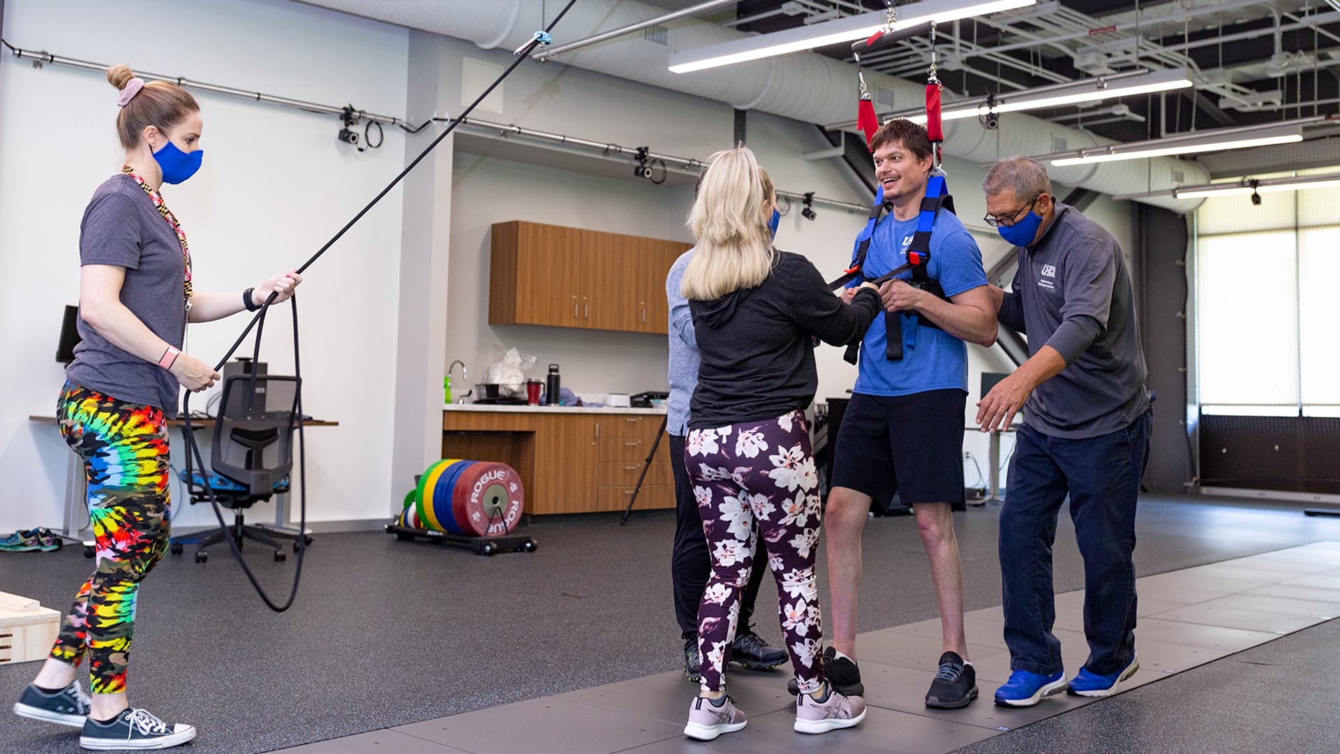 Sean Carter practices walking in a harness, supported on the right by HHPI Clinical Director Dr. Joe Hazzard, and guided by graduate students in UHCL's Exercise Sciences program.
